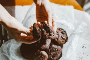 Close-up of hands breaking a tasty chocolate chip cookie with more cookies in the background.